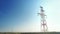 A power energy line of high-voltage transmission lines against a clear blue sky. The sun is shining through the pylon