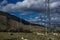 Power poles lines on yellow grassy steppe with green trees stand by slope of Baikal mountains. Metal constructions