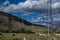 Power poles on yellow grassy steppe with green trees stand by slope of Baikal mountains. Metal constructions. Pine forest