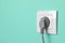 Power socket with inserted plug on turquoise wall, space for text. Electrical supply