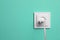Power socket with inserted plug on turquoise wall, space for text. Electrical supply