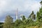 Power station in landscape. White and red long smoking chimney, industry and nature. Trees, grass, bushes and cloudy sky.