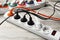 Power strip with extension cords on white wooden floor, closeup. Electrician\\\'s equipment