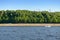 Powerboat sailing down the river along a concrete embankment with a green forest and tower cranes