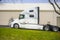 Powerful big rig semi truck tractor with rest compartment for truck drivers standing on the warehouse parking lot waiting for