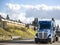 Powerful blue big rig bonnet semi truck tractor transporting cargo on step down semi trailer running on the wide highway with hill