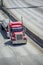 Powerful bright red classic big rig semi truck transporting covered commercial cargo on flat bed semi trailer running on the