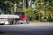 Powerful classic big rig semi truck with loaded flat bed semi trailer with covered and tightened cargo turning on the green forest