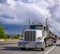 Powerful classic big rig white day cab semi truck transporting wire rolls on the flat bed semi trailer running on the multiline