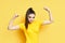 Powerful confident young woman showing arms muscles on yellow background