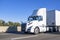 Powerful day cab white big rig semi truck with built-in roof spoiler transporting cargo in dry van semi trailer running on the