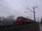 A powerful electric train travels fast on railway tracks on a foggy morning to the station