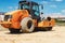 Powerful heavy road roller with a closed cabin against a blue cloudy sky. The skating rink prepares the ground for the