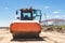 Powerful heavy road roller with a closed cabin against a blue cloudy sky. The skating rink prepares the ground for the