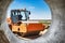 Powerful heavy road roller with a closed cabin against a blue cloudy sky. The skating rink prepares the ground for the