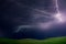 Powerful lightnings in dark stormy sky above green grass hills