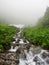 A powerful mountain stream flows down from the rocks in a dense fog
