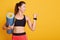 Powerful strong Caucasian woman raises arm, shows biceps, holding blue fitness mat for gym training, dresses sportwear, isolated