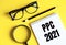 PPC 2021 Pay Per Click text written on a notebook with glasses, magnifying glass and pencil, on a yellow background