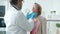 Practitioner in white gown and gloves examining young woman and talking to patient in clinic