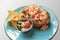 Prawns in a seafood dressing inside a baked, jacket potato on a blue plate with tortilla chips and a side salad in a small dish