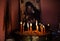 Prayer candles on a candlestick with sand, blurry image of an icon of the Virgin with child in the background.