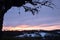 Prayer flags and offerings hang from the branches of an ancient pagan oak tree, silhouetted against a winter sunset in the English