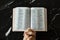 Praying hands folded in prayer to God Jesus Christ with open Holy Bible Book on dark granite background