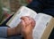 Praying : male hands clasped together on an open bible