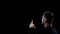 Praying man holding burning candle on dark background, spiritual ritual, faith