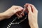 Praying on the rose garden, the hands of a young virgin with a rosary close-up on a black background