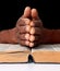 Praying to god with hands together on the bible Caribbean man praying with black background stock photo
