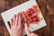 Pre-cooked bacon on white cutting board with womanâ€™s hand holding knife cutting bacon, on wood butcher block