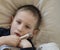 Pre-school sick boy lying in bed with a digital thermometer in hand and looking into camera