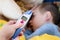 Pre-school sick boy lying on pillow in bed. Mother is measuring body temperature on his forehead with modern digital thermometer