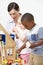 Pre-School Teacher And Pupils Playing With Wooden House