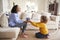 Pre-teen girl kneeling in front of her seated mother giving a handmade gift, a painted plant pot, side view