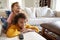 Pre-teen girl lying on sofa watching TV in the living room with her younger brother sitting on her back, close up