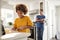 Pre-teen girl standing at worktop in the kitchen chopping, her father stands leaning in background smiling, selective focus