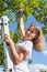 Pre-teen smiling Caucasian girl stretching to ripe red apple while standing ladder under apple tree