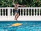 Pre-teens play in the pool by jumping on a small surfboard to keep their balance