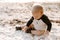 Precious Adorably Cute Happy Baby Boy Toddler Smiling and Playing in the Sand At the Beach Next to the Ocean Water Outside During