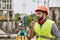 Precise measurements. Surveyor engineer in protective wear and red helmet using geodetic equipment and talking by walkie