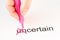 The prefix `un` of the word uncertain is crossed out with a pink pencil by a hand