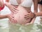 Pregnancy Asian woman and friends in bikini playing in transparent sea water. female hands touching pregnant belly.