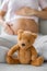 Pregnancy baby toy teddy bear and pregnant woman caressing her belly in background. Vertical crop