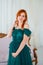 Pregnancy beauty. Beautiful elegant readhead pregnant woman in green dress posing in tender home interior.