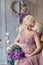 Pregnancy, motherhood and happy future mother concept - pregnant woman in airy violet dress with bouquet flowers against colorful