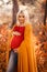 Pregnancy. Motherhood. Pregnant woman hugging her belly enjoying in autumn forest park. Beautiful blond woman in red knit sweater