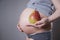Pregnancy and nutrition - pregnant woman with pear in hand on gray background